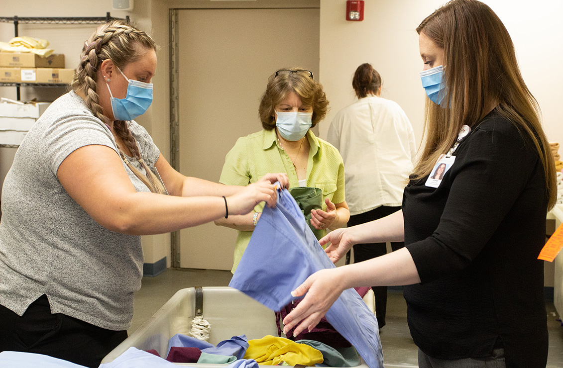Three women wearing masks and gloves work to fold linens together